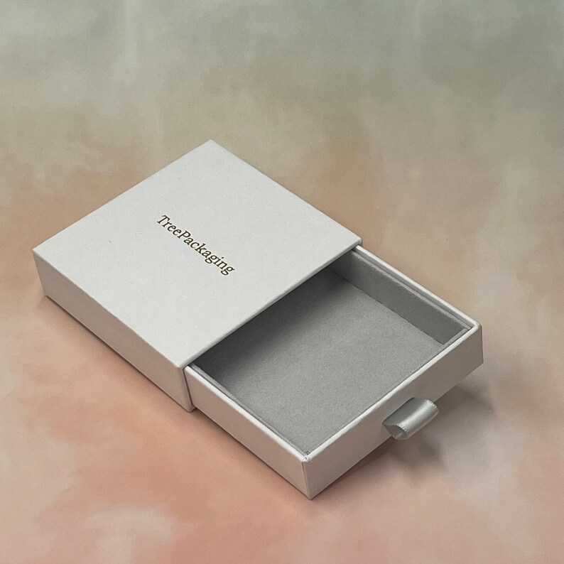 Puede incluir: Caja de caj&oacute;n blanca con interior gris y una leng&uuml;eta de tracci&oacute;n. La caja est&aacute; abierta y el texto "TreePackaging" est&aacute; impreso en la parte delantera.