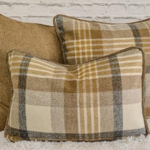 May include: Three rectangular scatter cushions featuring a mix of patterns and textures. One cushion has a solid tan herringbone weave, while the other two display a tan, cream, and charcoal grey plaid pattern. Each cushion is finished with brown piping.