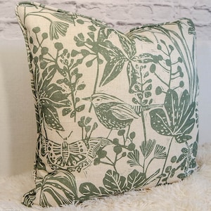 May include: A cream-colored pillow with a green floral pattern featuring birds, butterflies, and leaves. The pillow has a subtle linen texture.