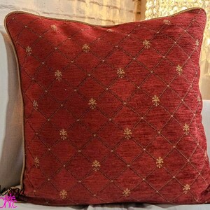 May include: Red cushion with a diamond pattern and gold accents. The cushion has a brown border.