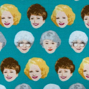May include: Teal fabric featuring a repeating pattern of illustrated faces with varying hairstyles and expressions. The faces are in shades of blonde, brown, and gray hair, with red lipstick and smiling faces. A fun and colorful design.