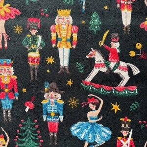 May include: Dark fabric featuring a festive pattern of Christmas illustrations. The design includes nutcrackers, ballerinas, toy soldiers, Christmas trees, and stars in various colours such as red, blue, yellow, and green.