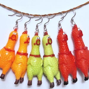 May include: Six dangling earrings featuring miniature rubber chicken figures in orange, lime green, and red. Each chicken has a textured surface, a wide-open mouth, and a small collar. The figures are suspended from silver-toned metal earring hooks.
