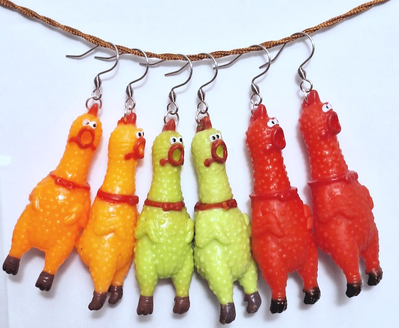 May include: Six dangling earrings featuring miniature rubber chicken figures in orange, lime green, and red. Each chicken has a textured surface, a wide-open mouth, and a small collar. The figures are suspended from silver-toned metal earring hooks.