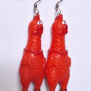 May include: A pair of dangling earrings featuring miniature red rubber chickens with textured skin, wide-open mouths, and white eyes. The chickens have black feet and are attached to silver-toned metal fishhook ear wires for pierced ears.