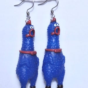 May include: A pair of dangling earrings featuring blue rubber chicken figures with textured skin, red combs, red beaks, and black feet. Each chicken has a wide-open mouth and is suspended from a silver-toned metal hook wire for pierced ears.