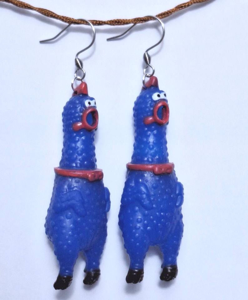 May include: A pair of dangling earrings featuring blue rubber chicken figures with textured skin, red combs, red beaks, and black feet. Each chicken has a wide-open mouth and is suspended from a silver-toned metal hook wire for pierced ears.