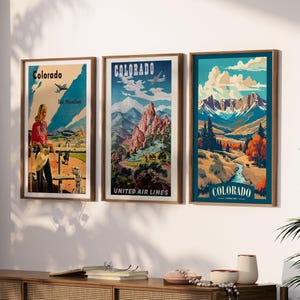 May include: Three framed vintage travel posters of Colorado. The posters feature illustrations of landscapes, mountains, and people. The posters are in wooden frames and are displayed on a white wall. The posters have the word "Colorado" on them.