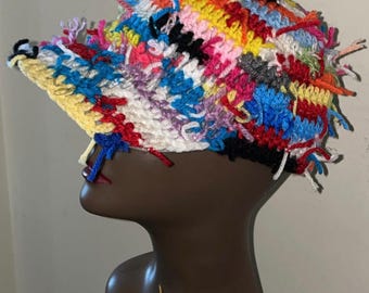 May include: A colorful crocheted hat with a long brim and a messy, frayed texture. The hat is made with a variety of colors, including red, blue, yellow, green, and pink.
