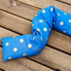 May include: A blue fabric neck pillow with gold polka dots. The pillow is shaped like a long, thin rectangle and is lying on a wooden surface.