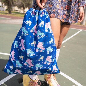 May include: A blue drawstring bag with a roller skate pattern. The bag has the text "Skate You Only Love" repeated on it. The bag is being held by a person wearing roller skates.