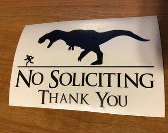 May include: White sign with black text and a silhouette of a running person and a dinosaur. The text reads "No Soliciting Thank You".