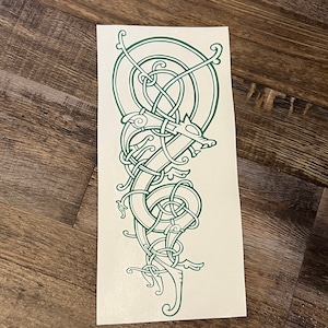 May include: A green line drawing of a wolf in a Celtic knot design. The wolf is facing right and has a long snout and pointed ears. The knotwork is intricate and detailed, and the design is symmetrical.