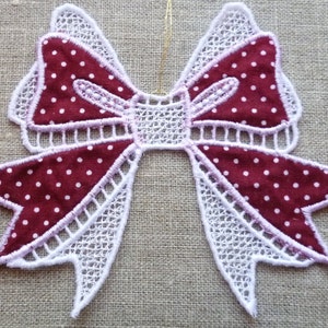 May include: A white lace bow with a red and white polka dot fabric centre. The bow is a decorative element for crafts and home decor.