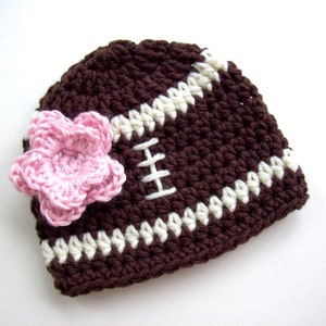 Peut inclure: Un chapeau de b&eacute;b&eacute; au crochet fait &agrave; la main en forme de ballon de football. Le chapeau est marron avec des rayures et des coutures blanches, et une fleur rose est attach&eacute;e sur le c&ocirc;t&eacute;. Le chapeau est pour les b&eacute;b&eacute;s.
