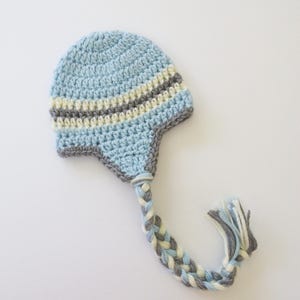 May include: A light blue crocheted baby hat with a long braided tail. The hat has white and gray stripes.