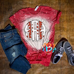K&ouml;nnte beinhalten: Rotes und wei&szlig;es Baseball-T-Shirt mit Used-Look-Design, mit einem kreisf&ouml;rmigen Grafik mit den Buchstaben "ARA". Das Shirt wird mit blauen Jeans und grauen Turnschuhen kombiniert, alles auf einer Holzoberfl&auml;che angeordnet.
