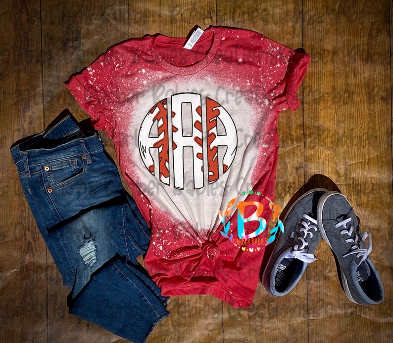 K&ouml;nnte beinhalten: Rotes und wei&szlig;es Baseball-T-Shirt mit Used-Look-Design, mit einem kreisf&ouml;rmigen Grafik mit den Buchstaben "ARA". Das Shirt wird mit blauen Jeans und grauen Turnschuhen kombiniert, alles auf einer Holzoberfl&auml;che angeordnet.