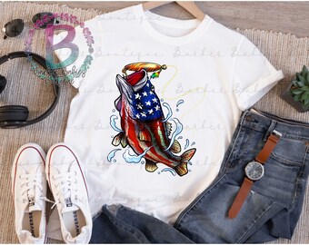 May include: White t-shirt featuring a graphic of a fish with an American flag design. The fish is red, white, and blue, with a fishing lure in its mouth. The shirt is displayed with blue jeans, a watch, and white sneakers.