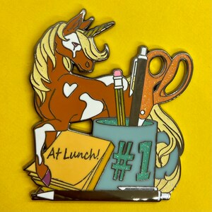 May include: A brown and white unicorn with a gold horn is holding a blue mug with the number 1 on it. The mug is surrounded by a pencil, a pair of scissors, and a note that says "At Lunch!"