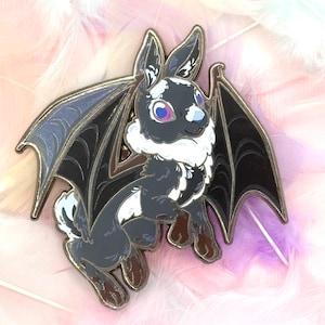 May include: A black and white enamel pin of a bat-eared bunny with large wings. The bunny has pink eyes and a white nose. The wings are black with a purple iridescent sheen.