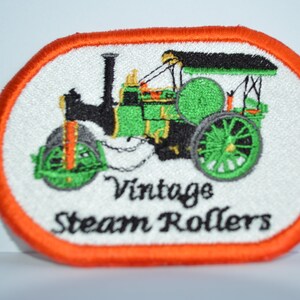 May include: An embroidered patch with an orange border, featuring a vintage green and black steamroller with the text "Vintage Steam Rollers".