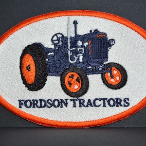 Może przedstawiać: Naszywka haftowana przedstawiająca zabytkowy traktor Fordson w kolorze niebieskim i pomarańczowym z napisem "Fordson Tractors".