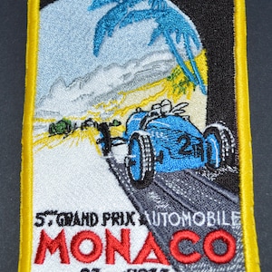 May include: A vintage embroidered patch featuring a blue race car speeding down a road with palm trees in the background. The text "5. GRAND PRIX AUTOMOBILE MONACO 23 avril 1933" is embroidered in white, red, and black.