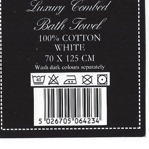 K&ouml;nnte beinhalten: Schwarz-wei&szlig;es Etikett mit dem Text "Luxury Combed Bath Towel", "100% COTTON", "WHITE", "70 X 125 CM" und "Wash dark colours separately". Das Etikett enth&auml;lt auch einen Barcode und Waschanweisungen.