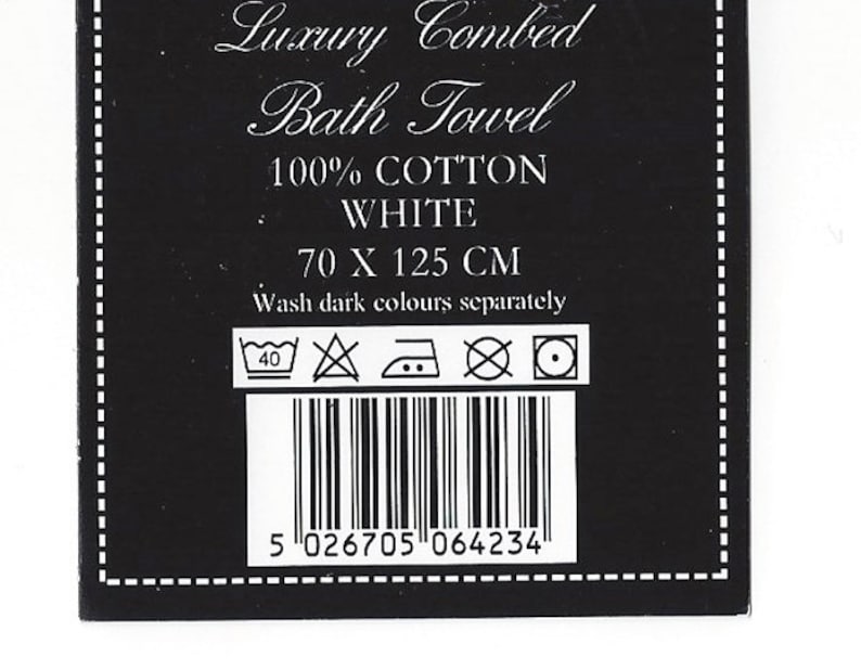 K&ouml;nnte beinhalten: Schwarz-wei&szlig;es Etikett mit dem Text "Luxury Combed Bath Towel", "100% COTTON", "WHITE", "70 X 125 CM" und "Wash dark colours separately". Das Etikett enth&auml;lt auch einen Barcode und Waschanweisungen.