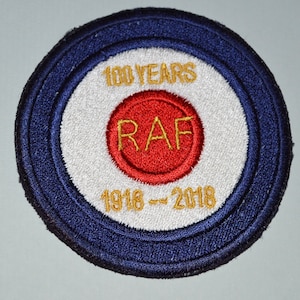May include: A blue and white round patch with a red circle in the center. The red circle has the letters "RAF" in gold lettering. The patch has the text "100 YEARS 1918 - 2018" in gold lettering.
