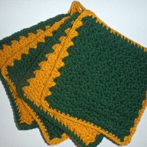 Op de afbeelding: Set van vier gehaakte ovenwanten in groen en goud. De ovenwanten zijn vierkant met een groen midden en een gouden rand.