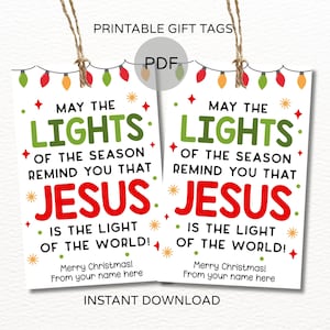 Puede incluir: Dos etiquetas de regalo imprimibles blancas con el texto "May the Lights of the Season Remind You That Jesus is the Light of the World!" en verde y rojo. Las etiquetas están decoradas con luces navideñas y estrellas.