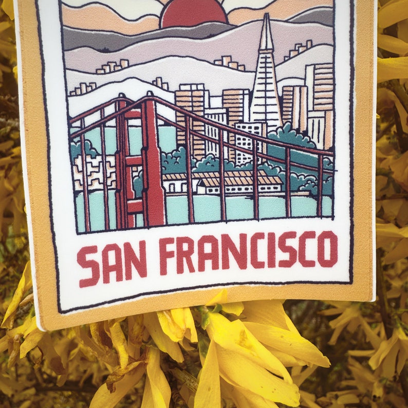 May include: A yellow and white sticker with a cartoon illustration of the Golden Gate Bridge and the San Francisco skyline. The sticker says "SAN FRANCISCO" in red letters.