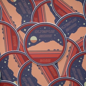 Puede incluir: Una colección de pegatinas circulares con un diseño retro. Cada pegatina tiene un fondo azul oscuro con las palabras "OLYMPUS MONS" y "2082". El diseño incluye una cordillera, un sol poniente y estrellas, con rayas rojas y naranjas.