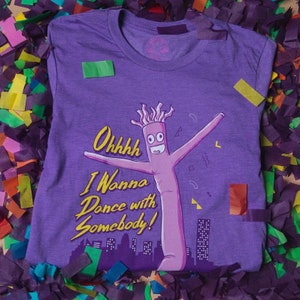 May include: Purple t-shirt with a cartoon inflatable tube man wearing a silly expression. The text on the shirt reads "Ohhhhh I Wanna Dance with Somebody!"