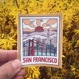 May include: A sticker with a retro illustration of the Golden Gate Bridge and the San Francisco skyline. The sticker has a yellow background and the text "San Francisco" in red.