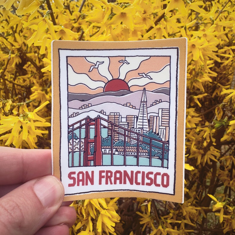 May include: A sticker with a retro illustration of the Golden Gate Bridge and the San Francisco skyline. The sticker has a yellow background and the text "San Francisco" in red.