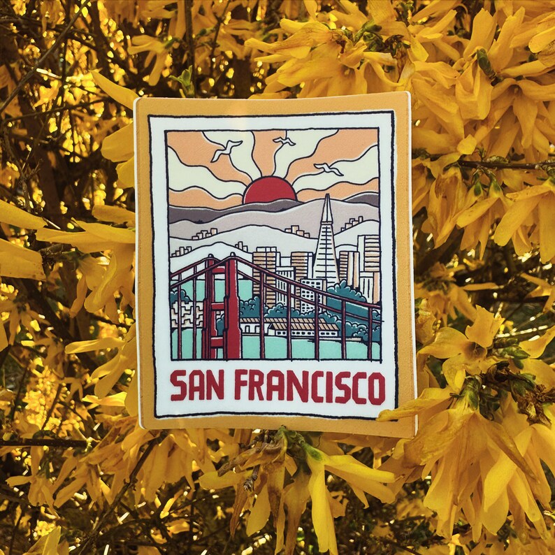 May include: A yellow sticker with a retro illustration of the Golden Gate Bridge and the San Francisco skyline. The illustration is set against a sunset with a red sun and the text "San Francisco" at the bottom.
