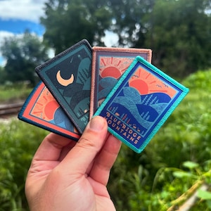 Puede incluir: Cuatro parches bordados coloridos con escenas de la naturaleza. Los parches presentan una puesta de sol, una luna y una cordillera. El texto "BLUE RIDGE MOUNTAINS" está en uno de los parches.
