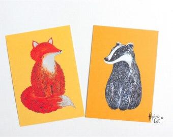 May include: Two greeting cards with animal illustrations. One card features a red fox with closed eyes, the other a badger with black and white fur. Both cards have a yellow background.
