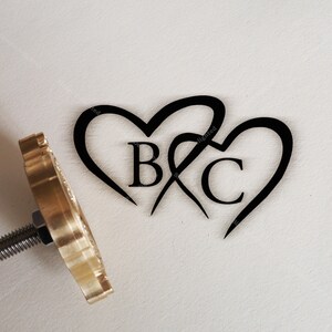 Könnte beinhalten: Ein Stempel aus Messing mit einem Griff und zwei ineinander verschlungenen Herzen mit den Initialen "B & C" darin.