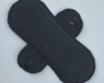 May include: A dark gray reusable menstrual pad with a contoured shape. The pad features a quilted design and two sets of snap closures for secure wear. The pad is made of a soft, absorbent material.