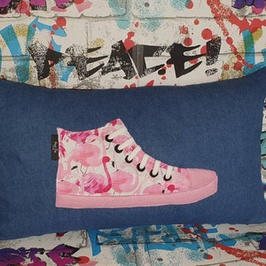 K&ouml;nnte beinhalten: Ein blaues Jeans-Kissen mit einem pinkfarbenen Flamingo-Druck-High-Top-Schuh-Design. Der Schuh ist pink mit schwarzen Schn&uuml;rsenkeln und einer wei&szlig;en Sohle.