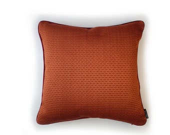 Puede incluir: Una almohada de color óxido con tejido texturizado y ribete burdeos. La almohada tiene una cremallera oculta.