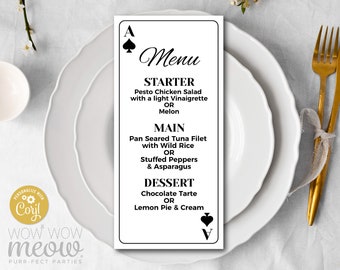 May include: A menu card in the shape of a playing card, featuring the Ace of Spades and the Ace of Clubs. The menu lists starter, main, and dessert options. The text includes "Menu", "Starter", "Main", and "Dessert". The card is on a white plate.