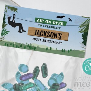 Puede incluir: Una bolsa de fiesta verde y azul con un diseño de tirolina. La bolsa tiene una etiqueta que dice "Zip on over to celebrate Jackson's 10th Birthday!" y un logotipo personalizado que dice "Personalize with Coryl".