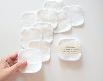 May include: White cotton rounds with a stitched edge, arranged in a pile on a white surface. A hand holds one round. A label reads "Emillia Design Cotton Rounds made in USA of imported fabric."