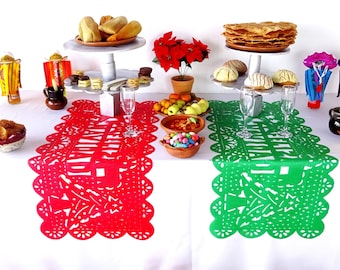May include: A white tablecloth with two colorful paper table runners, one red and one green. The table is set with a tiered cake stand with pastries, a bowl of fruit, and a bowl of candy. There are also two glasses of champagne and a variety of decorative items, including pinatas and figurines.