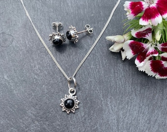 May include: A silver necklace and earrings set with black gemstone pendants. The pendants are surrounded by a silver sunburst design.